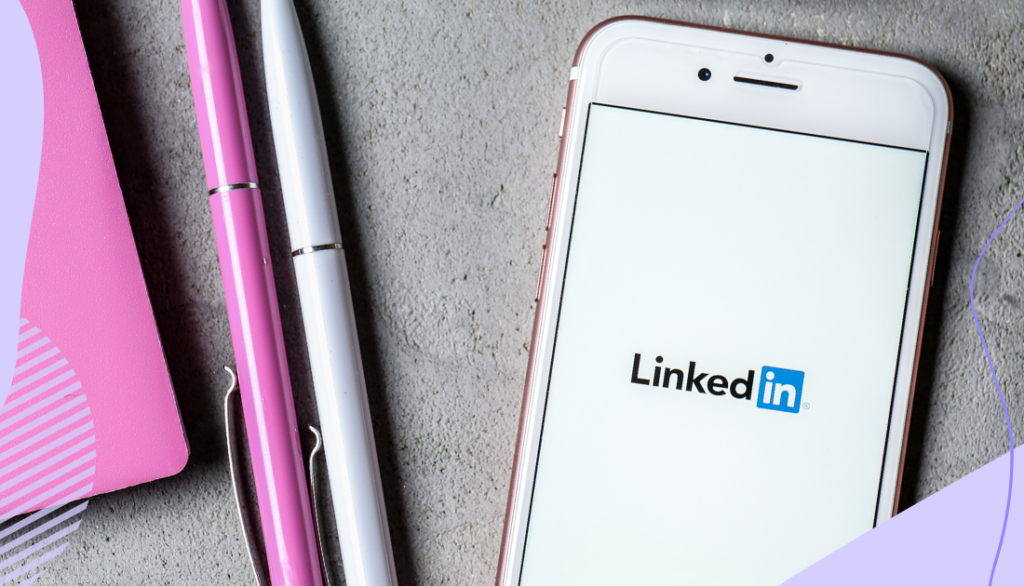 A mobile phone with the LinkedIn logo on the screen along with pens and a notebook on a desk.