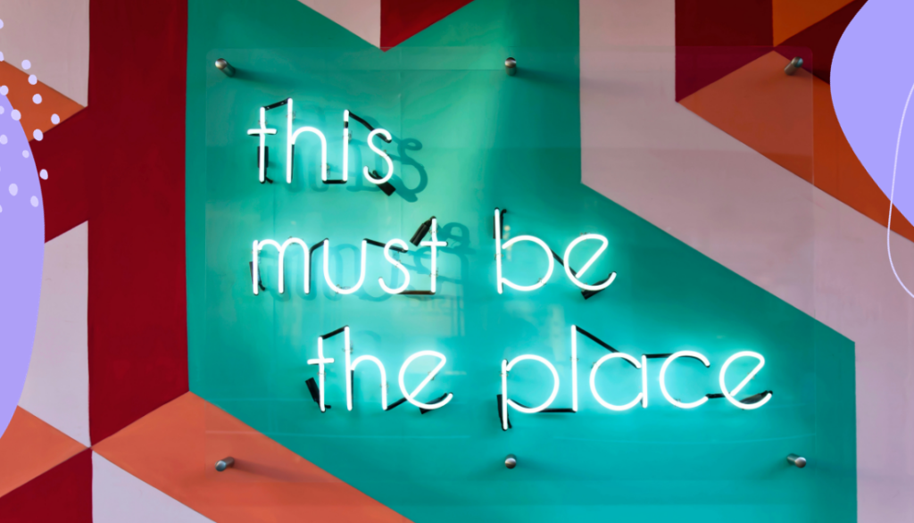A neon sign that says 'This must be the place' with geometric shapes in the background.