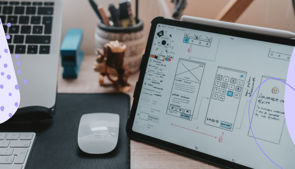 Laptop, tablet, and mouse on a design with wireframes of a mobile app on the tablet.